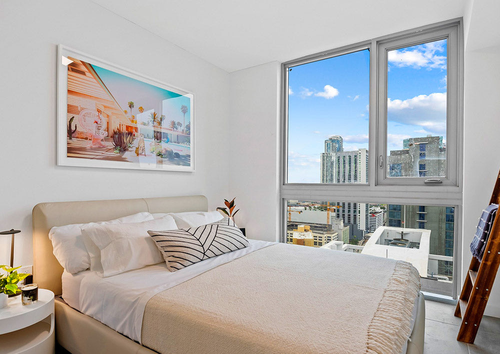 Image of tropical art in a bedroom featuring a large open window looking out at the city.